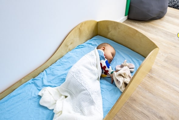 A baby is sleeping in a wooden crib.