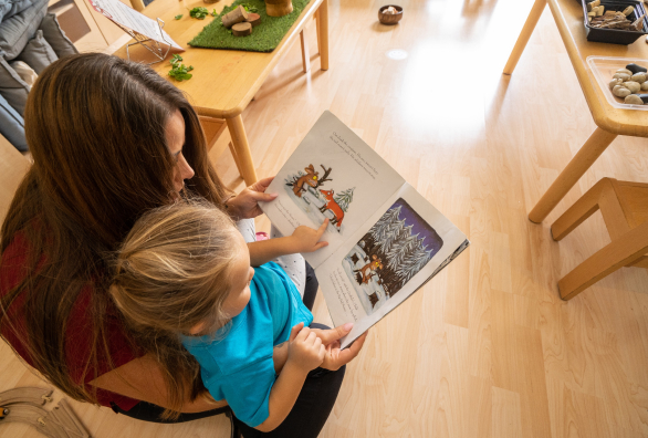 A woman reading a book to a child in a playroom.