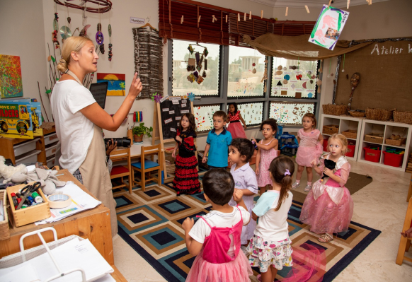 A woman in a dress is teaching children in a classroom.