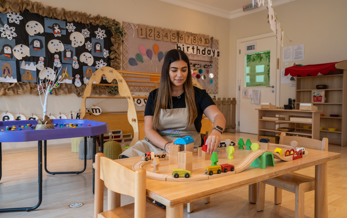 A woman in an apron playing with toys in a playroom.