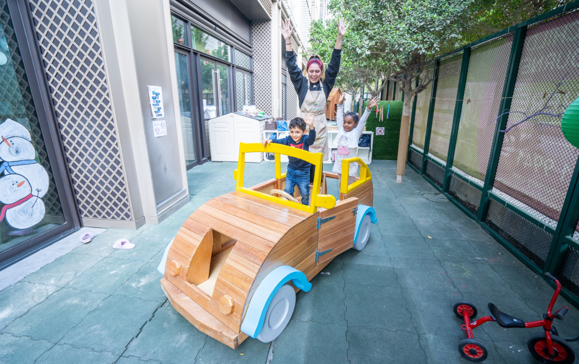 A child is riding in a wooden toy car.