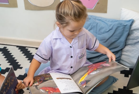 Two young girls sitting on the floor reading a book.