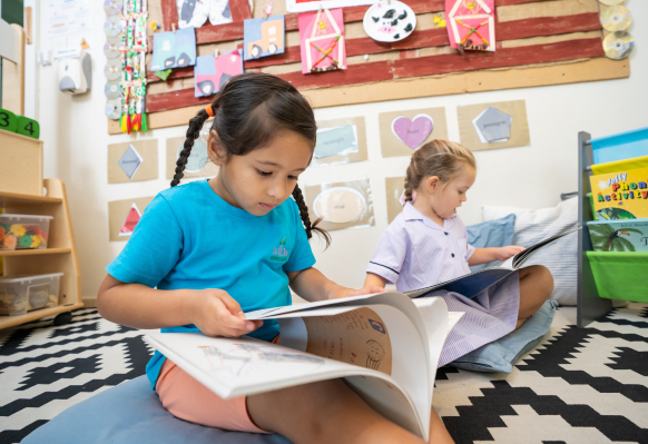 Two young girls reading a book in a classroom.